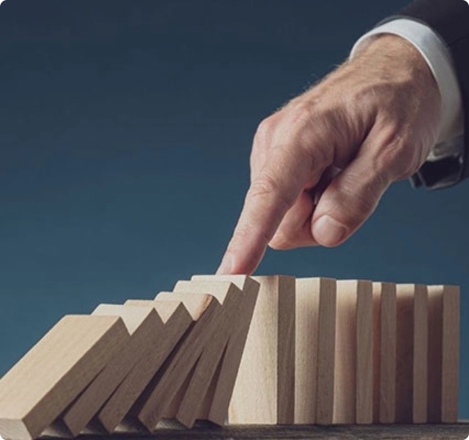 Mano che ferma una reazione a catena di tessere domino in legno.