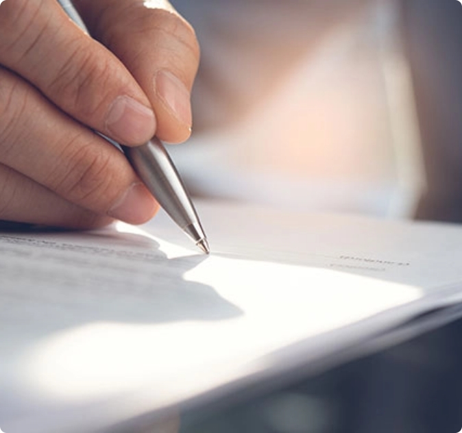 Mano che firma un documento con una penna argentata su un foglio bianco.