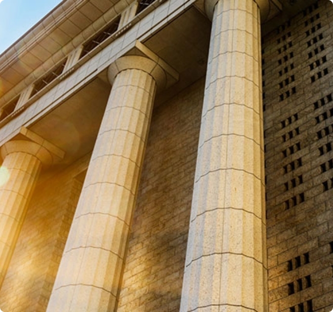 Colonne in pietra di un edificio istituzionale viste dal basso con luce solare sullo sfondo.