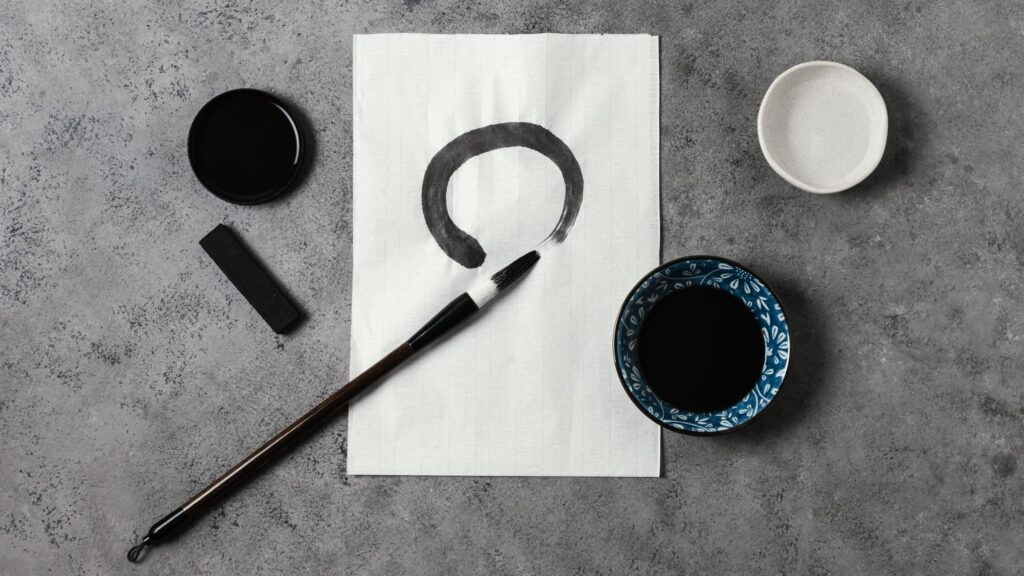 Pennello e inchiostro accanto a un cerchio Enso dipinto su carta di riso, con utensili per pittura giapponese.